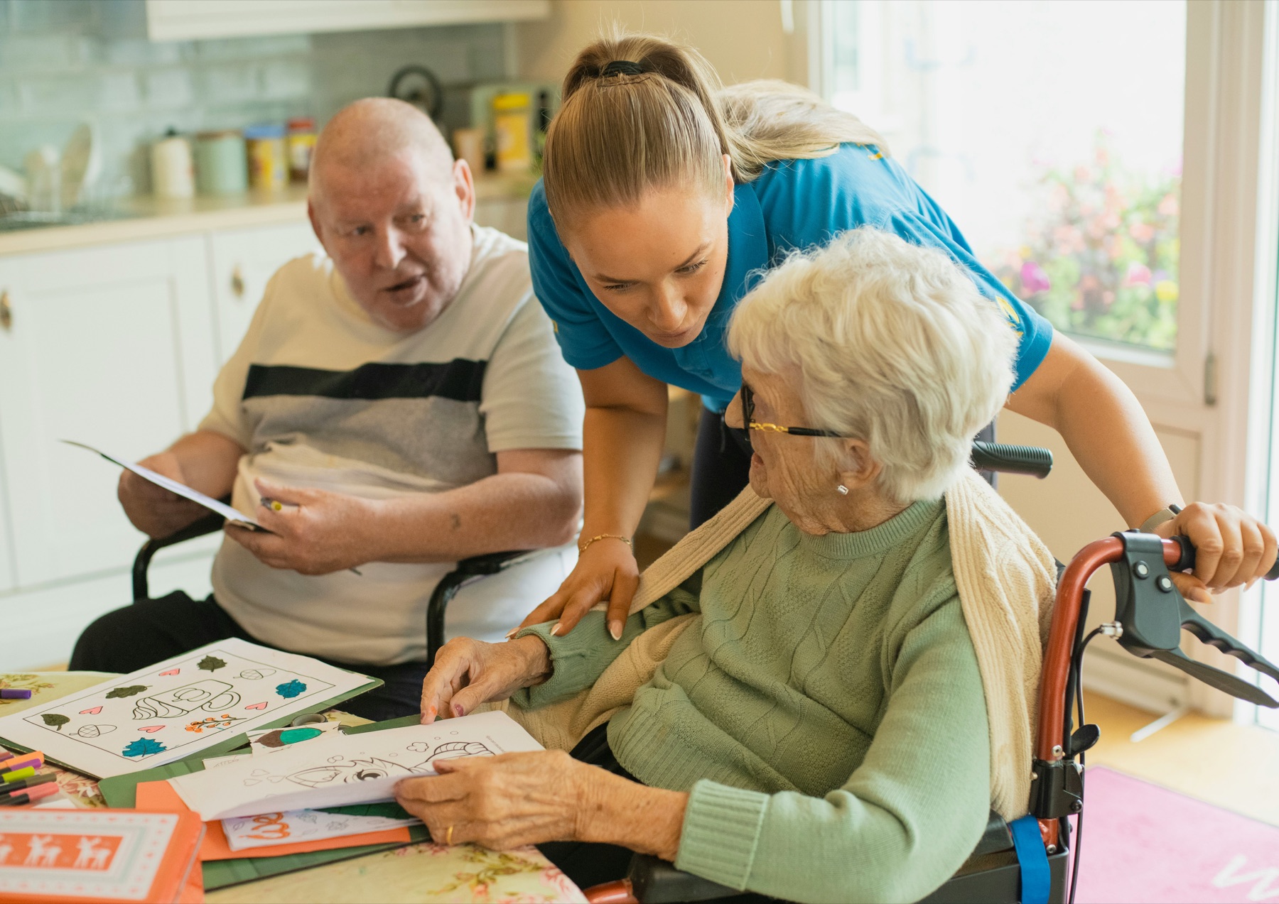 A home care professional spending time with two older adults at a kitchen table